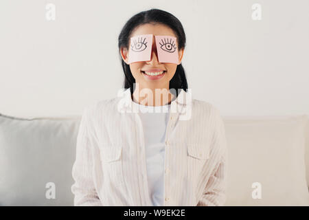 smiling latin woman with eyes covered with sticky notes with drawn eyes Stock Photo