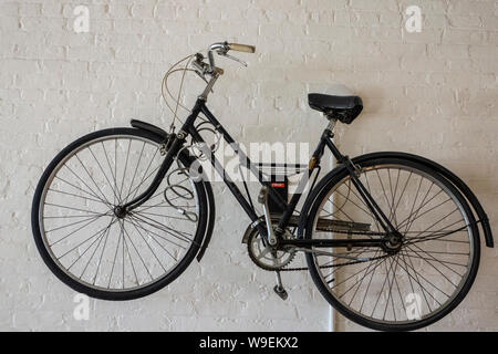 Black women's bicycle hanging on a white painted brick wall Stock Photo