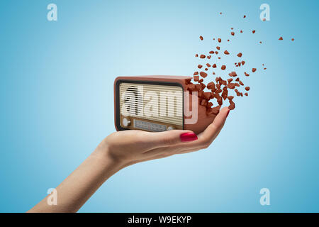 Female hand holding old radio set shattering into pieces on blue background Stock Photo