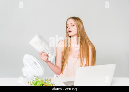 beautiful girl suffering from heat and waving newspaper on grey Stock Photo