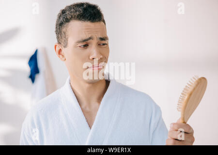 disappointed young man in bathrobe holding hairbrush Stock Photo