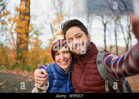 Couple of Canadian millennials taking selfies with a smartphone in a fall forrest Stock Photo