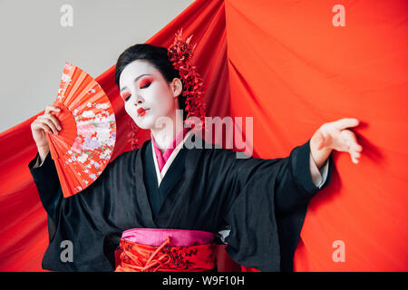 beautiful geisha in black kimono with hand fan and red cloth on background dancing isolated on white Stock Photo