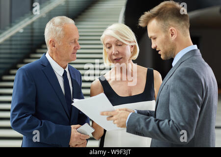 Young businessman holding document showing it to his colleagues and they discussing in team at modern office Stock Photo