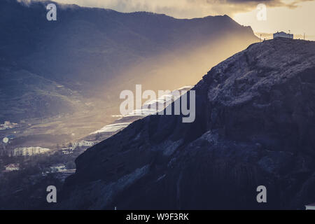 Image of solar panels on a hill with sunset sunlight breaking through clouds creating epic atmosphere, Madeira Stock Photo