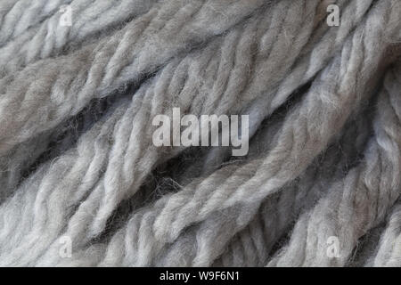 Woolen fluffy threads or tassels from scarf, macro. Soft grey merino wool backdrop, closeup. Autumn and winter flat lay. Scandinavian minimal style. Stock Photo