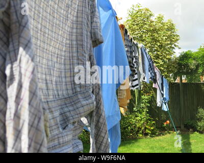 A washing-line of clothes hung out with pegs on a clothesline to dry in an English garden. Stock Photo