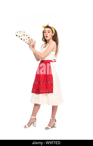 full length view of young shocked housewife in dress and apron holding oven mitten isolated on white Stock Photo