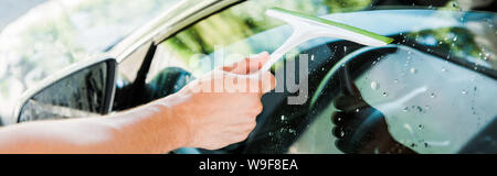panoramic shot of man holding squeegee while cleaning car window Stock Photo