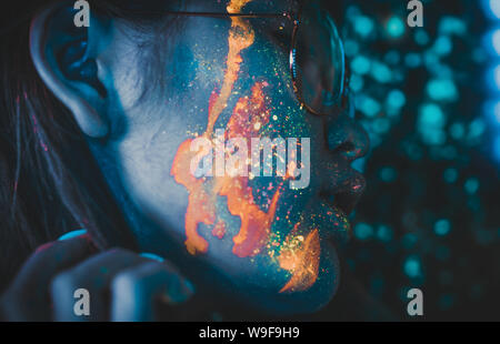 Beautiful young woman dancing and making party with fluorescent painting on her face. Neon facial portraits Stock Photo