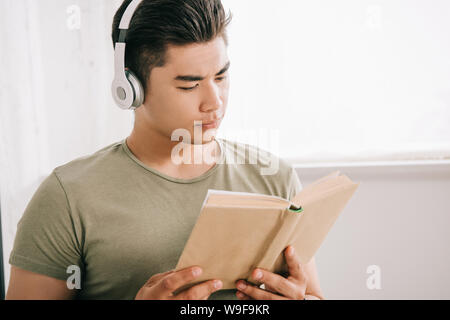 young asian man reading book while listening music in headphones Stock Photo
