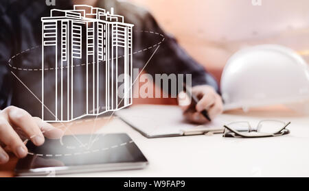 Young blurred architect sitting in the office and designing new building, with digital drawing on tablet PC and paper sketch. Architecture, building a Stock Photo