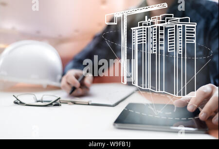 Young blurred architect sitting in the office and designing new building, with digital drawing on tablet PC and paper sketch. Architecture, building a Stock Photo