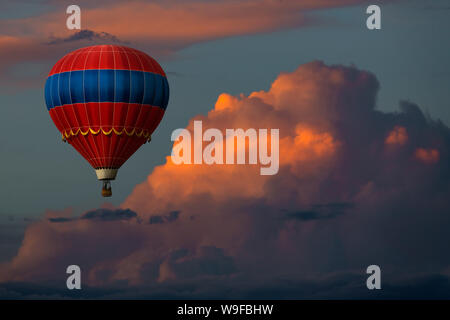 Red hot air balloon floating in beautiful colourful storm clouds at sunset Stock Photo
