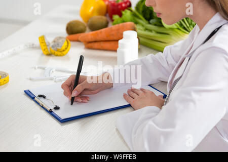 cropped view of dietitian in white coat writing in clipboard at workplace Stock Photo