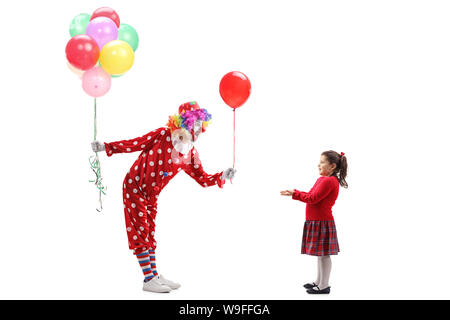 Full length profile shot of a clown giving a balloon to a little girl and holding a bunch of balloons isolated on white background Stock Photo