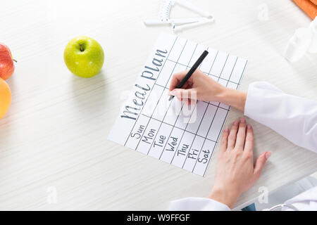 cropped view of dietitian writing in meal plan at table with fruits Stock Photo