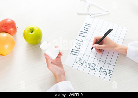 cropped view of dietitian holding pills and writing in meal plan at workplace Stock Photo