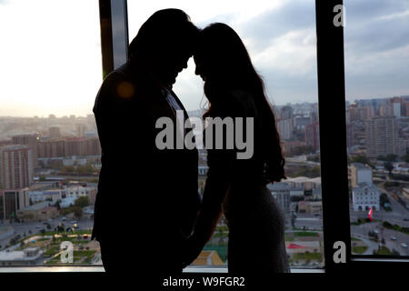 Silhouette of bride beautiful young woman and groom handsome man share love head to head on background of window . The bride and groom in a cozy house Stock Photo