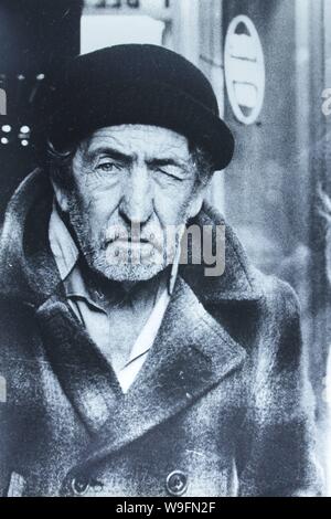 Fine black and white art photography from the 1970s of an elderly man staying warm while bundled up in a winter hat and coat. Stock Photo