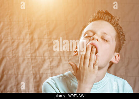 the boy in the blue t-shirt is tired, wants to sleep and yawns Stock Photo