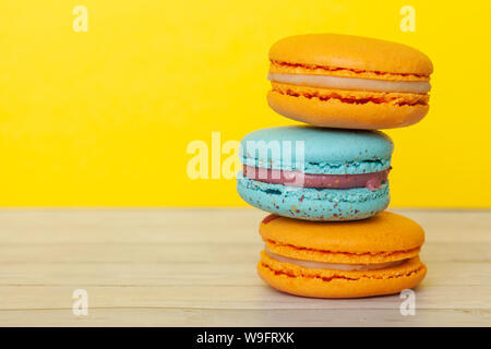 Orange and blue macaroons on yellow background, French cookies as a treat for the holiday Stock Photo