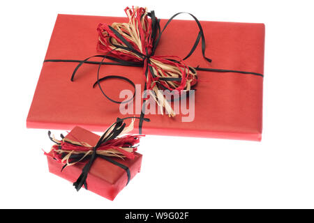 Two gifts wrapped in plain red paper with a raffia bow are set on a white background. Horizontal shot. Isolated on white. Stock Photo