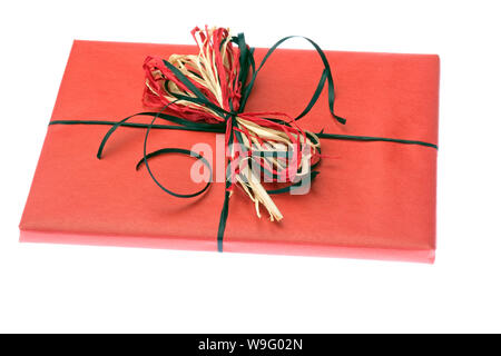 A gift wrapped in plain red paper with a raffia bow are set on a white background. Horizontal shot. Isolated on white. Stock Photo
