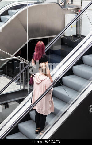 two women riding an escalator at a shopping mall or shopping centre Stock Photo