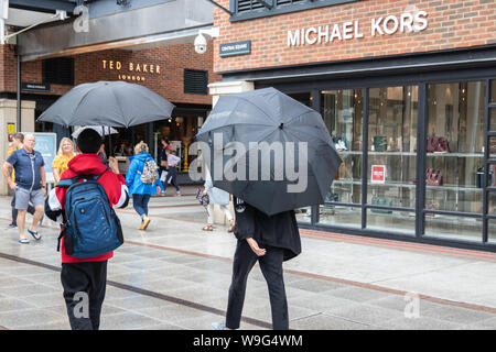 Two young men taking shelter from the rain holding umbrellas whilst shopping at a shopping centre Stock Photo