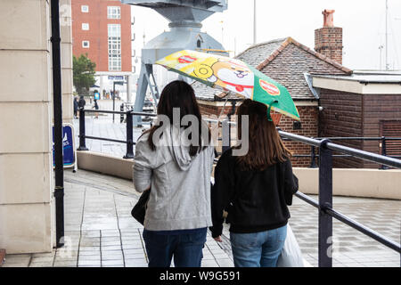 Two women taking shelter from the rain under one umbrella