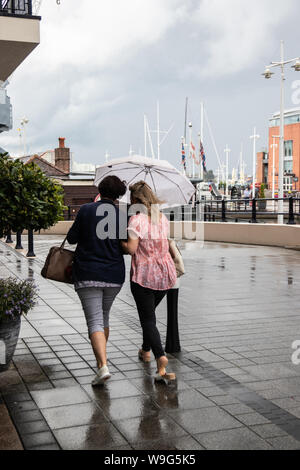 Two women taking shelter from the rain under one umbrella