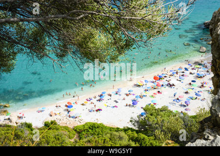 (Selective focus) View from above, blurred beach full of beach umbrellas and people sunbathing and swimming on a turquoise water. Cala Gonone, Italy. Stock Photo