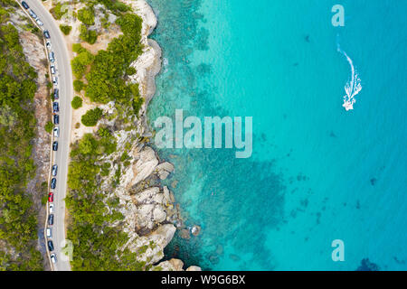 View from above, stunning aerial view of a road that runs along a rocky coast bathed by a turquoise and transparent sea. Cala Gonone, Sardinia, Italy. Stock Photo