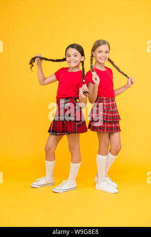 Cheerful friends. Cute little girls smiling yellow background. Happy small girls wearing same outfits. Friends enjoying friendship. Playful kids. Happy together. School friends having fun together. Stock Photo