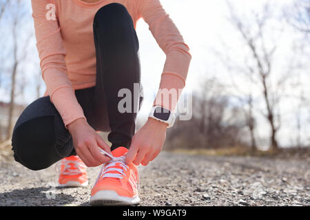Running shoes and runner sports smartwatch. Female runner tying shoe laces on running trail using smart watch heart rate monitor. Stock Photo