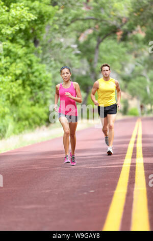 Running Health and fitness. Runners on run training during fitness workout outside on road. People jogging together living healthy active lifestyle outside in summer. Full body length of woman and man Stock Photo