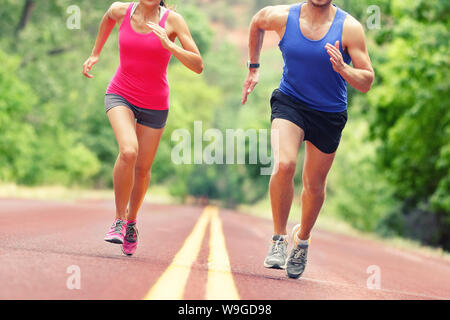 Low section of determined man and woman running on country road. Young couple is in sports clothing. They are representing their healthy lifestyle. Stock Photo