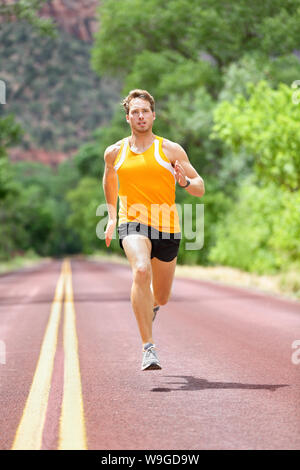 Full length of determined man running on country road. Young male is in sports clothing. He is representing fit and healthy lifestyle. Stock Photo