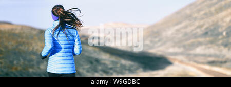 Winter running woman on trail run outdoors in snowy mountains background. Panoramic banner with copy space on white snow. Stock Photo