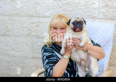 Happy smiling mature woman with pet dog outdoors.Happy middle age woman playing with bulldog on backyard in sunset light, summer vacation. Lady with funny resting, hugging and having fun, cute moments Stock Photo
