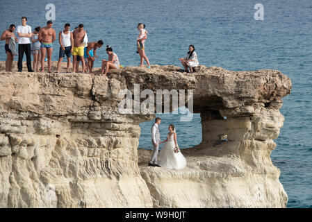 People standing and sitting on the rocks, enjoying the crystal clear waters and a young married couple get photography Stock Photo