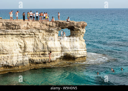 People standing and sitting on the rocks, enjoying the crystal clear waters and a young married couple get photography Stock Photo