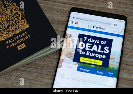 Air Transat website on a smartphone along with a Canadian Passport placed on a table. Stock Photo