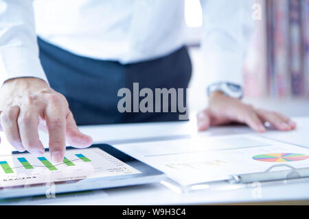 Business man touching a tablet touch screen analysing on business performance reports and returning on investment, ROI, or investment risk analysis. Stock Photo