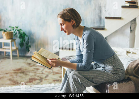 Young woman reading book on stairs in the loft art work studio room, slow life Stock Photo