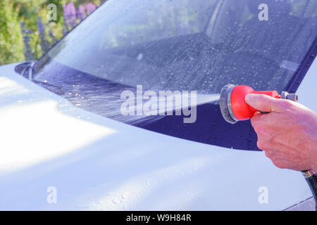 Car warhing. Worker cleaning white car on open air.Cleaning Car Using High Pressure Water. Man washing his car under high pressure water in service Stock Photo
