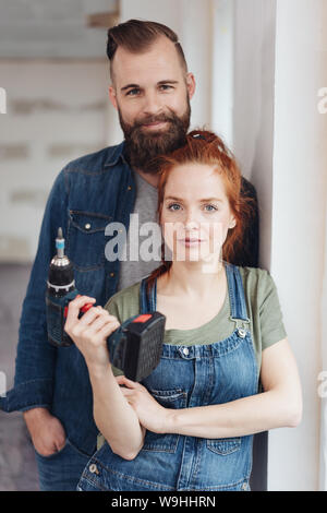 Capable young couple doing DIY renovations to their new home posing together with the woman holding an electric drill in her hand