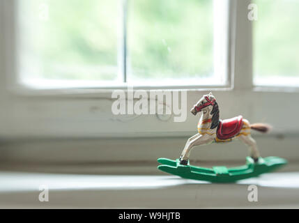 wooden antique miniature rocking horse swinging in the window sill of an old white wooden window