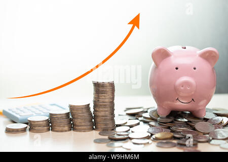 Saving money concept.business rich income show as stack money coin growing arrow with piggy bank smile over coins pile. Stock Photo